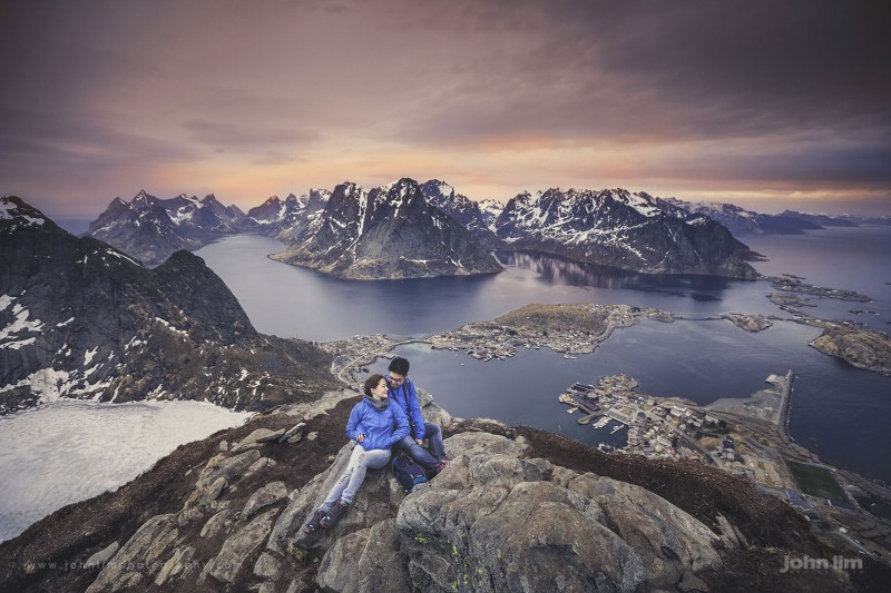 adventurous couple in hiking gear on top of Reinebringen in Lofoten Islands Norway, overlooking the islands with gorgeous sunset