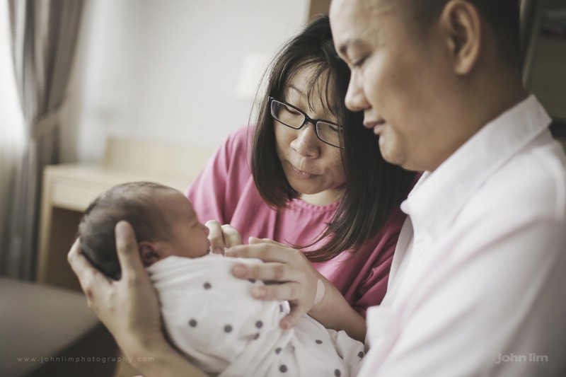 first day in the world of this newborn baby boy, first 24 hours at hospital, held lovingly by father with mother looking playfully at baby